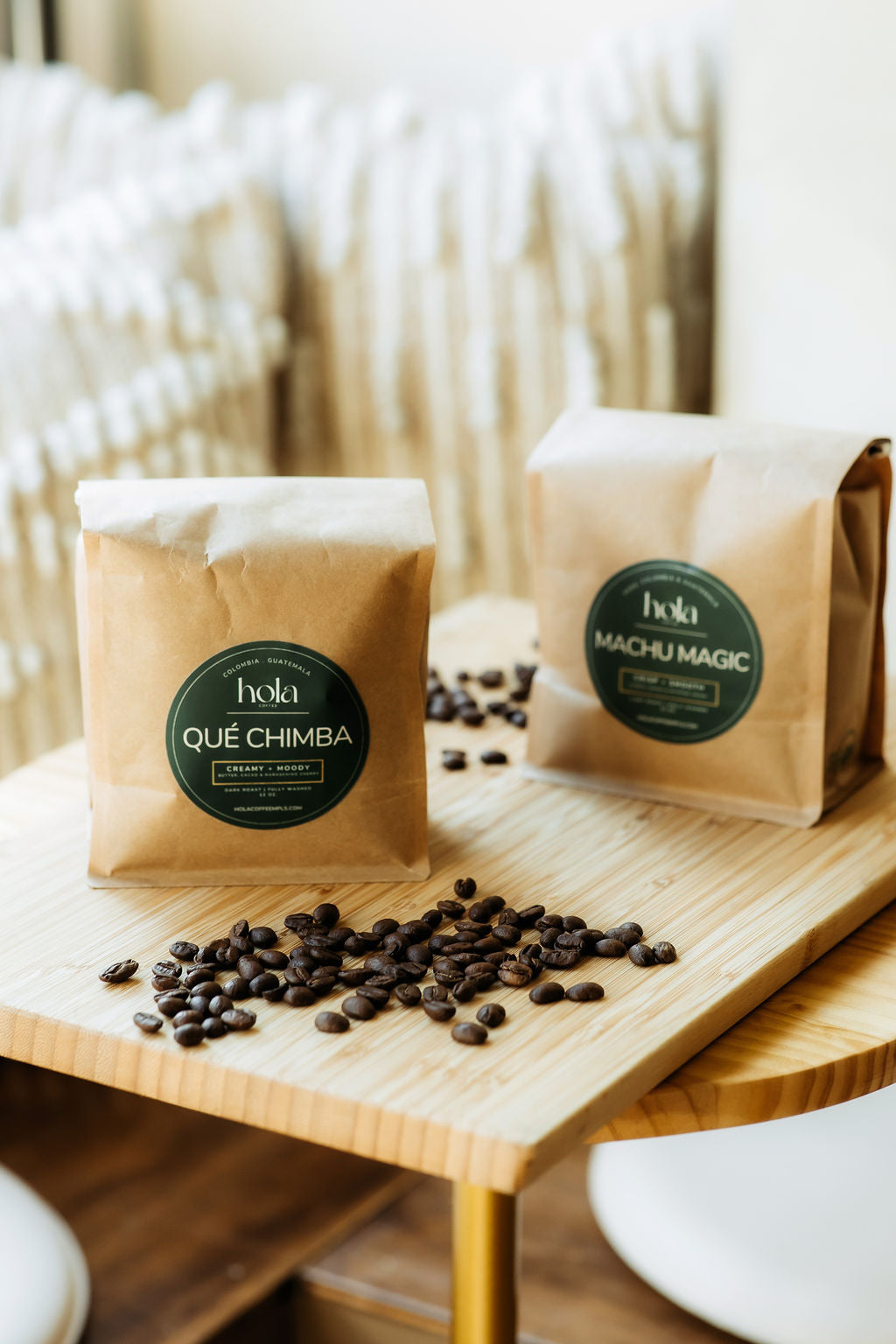 Qué Chimba and Machu Magic coffee bags on a wooden table with scattered coffee beans