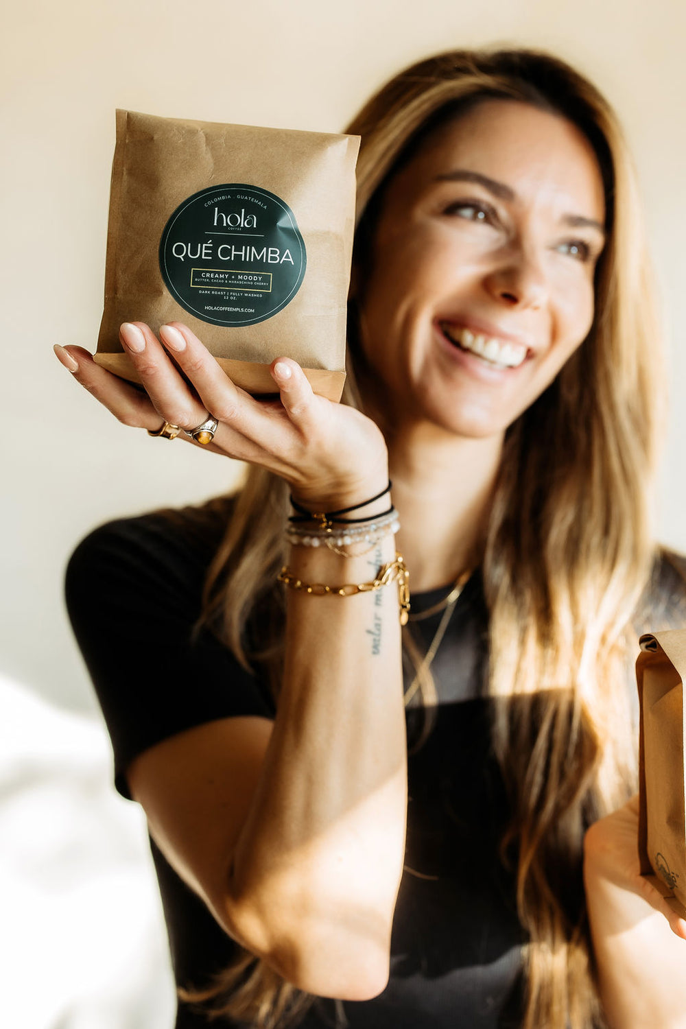 A smiling person holding a Qué Chimba coffee bag