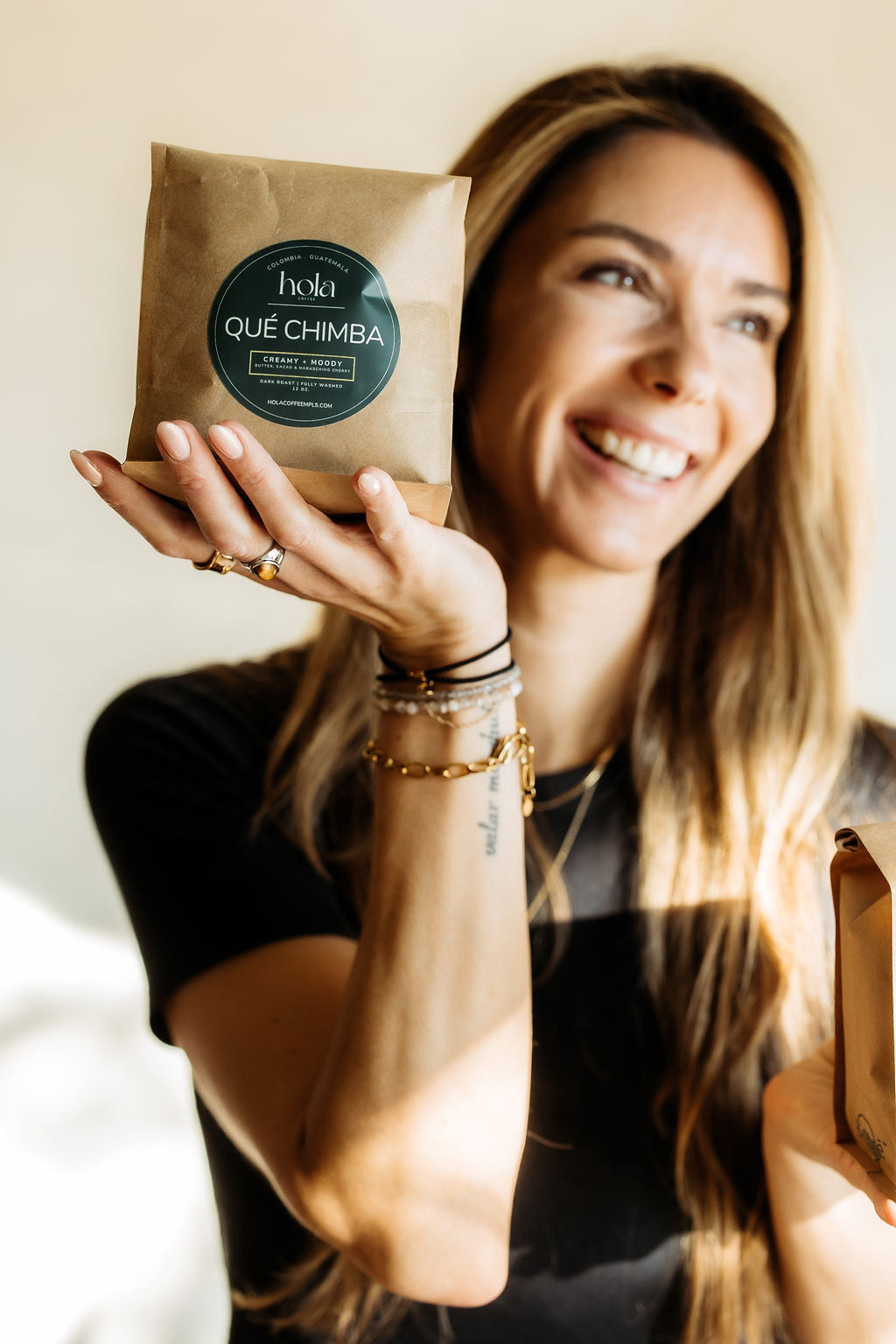 A smiling person holding a Qué Chimba coffee bag